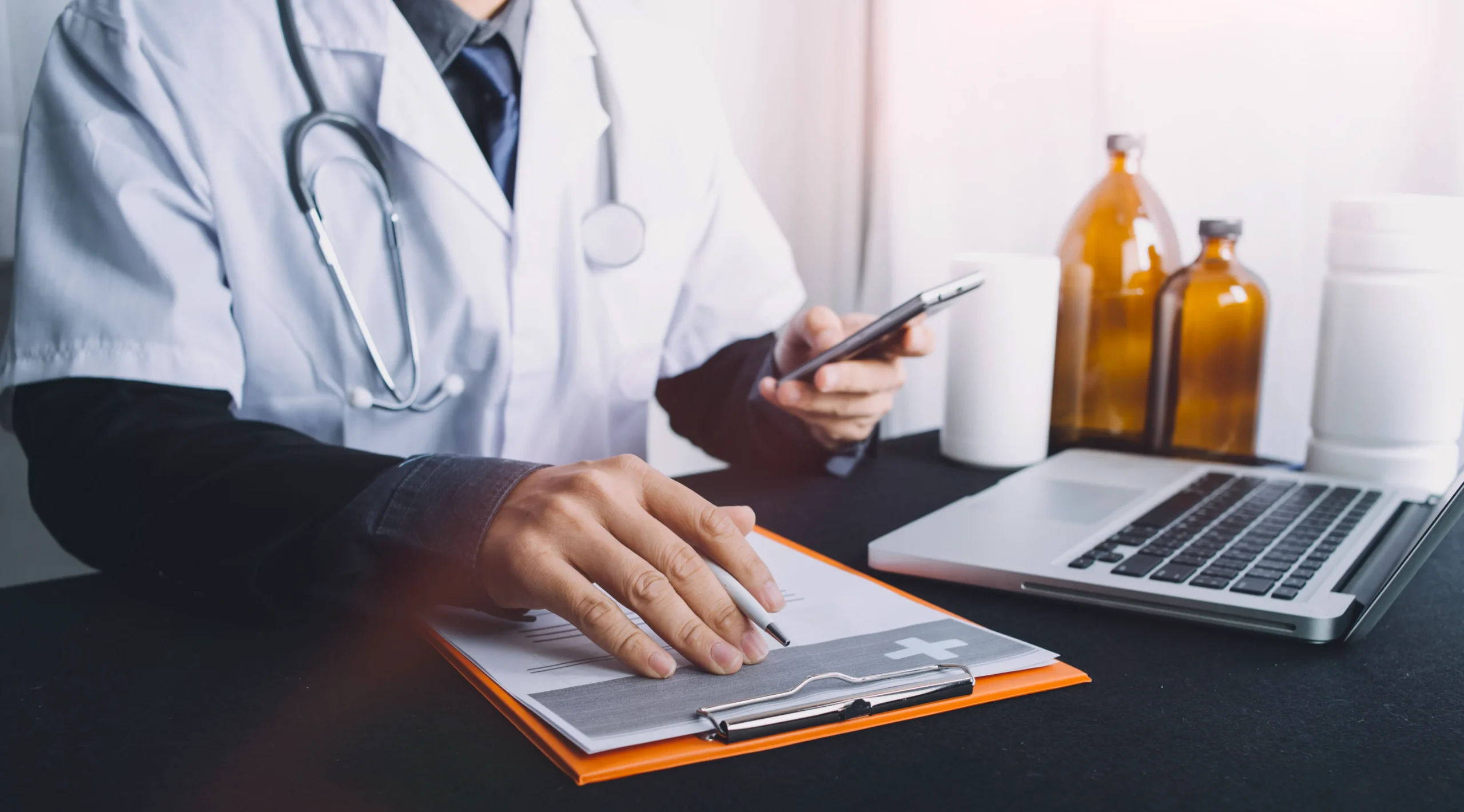 A medical professional cross-referencing mobile data with a clipboard to coordinate healthcare risk management and healthcare compliance management.