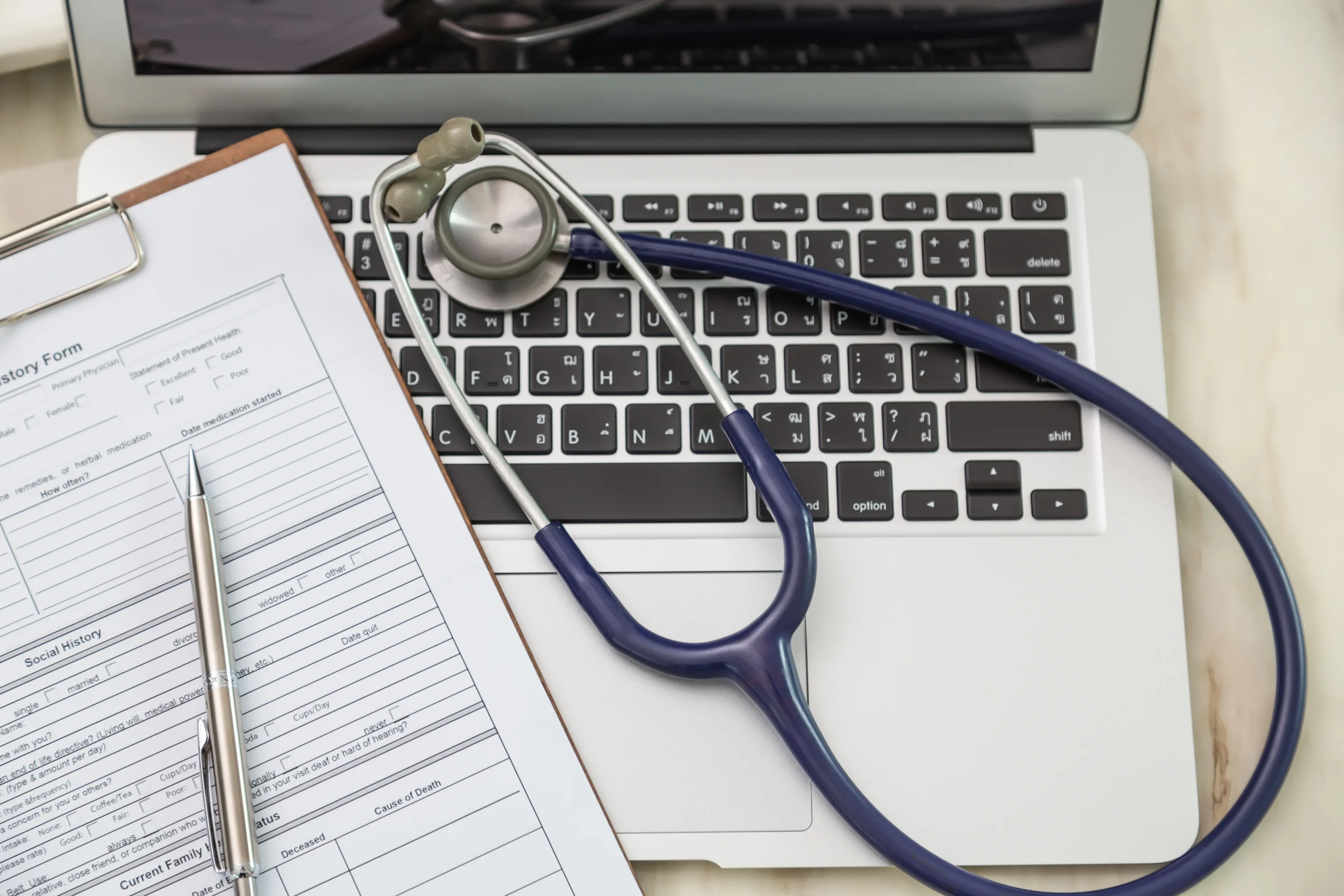 Medical clipboard form and stethoscope resting on a laptop keyboard to track healthcare regulations.