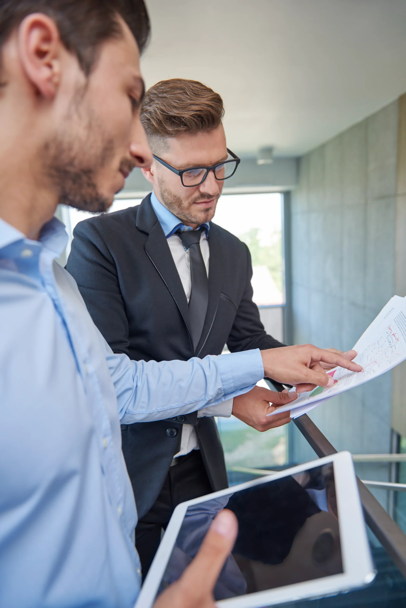 Two professional colleagues standing together reviewing a printed paper document and data on a digital tablet, preparing their organization for an upcoming Healthcare Compliance Audit.