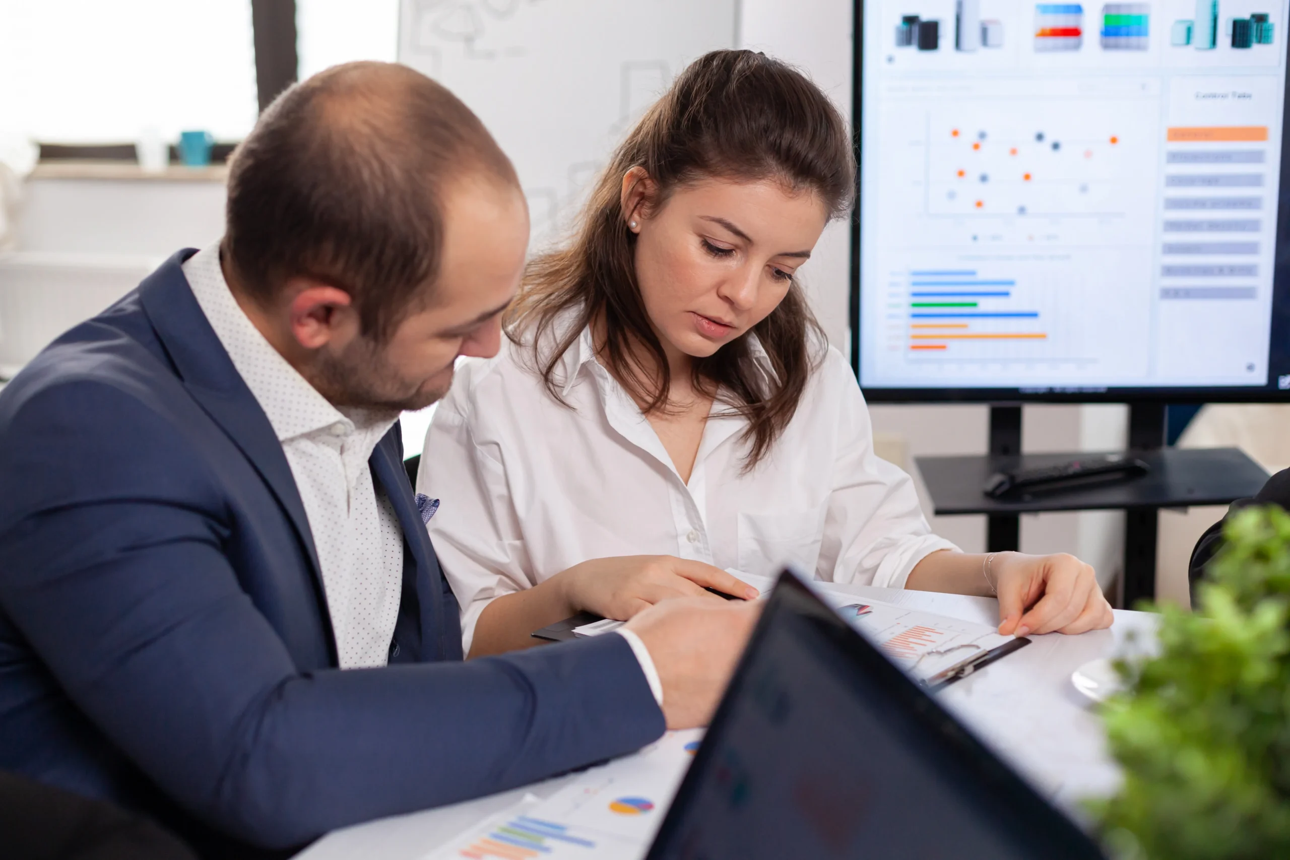 Analysts reviewing paper reports beside a digital data dashboard powered by healthcare compliance software.