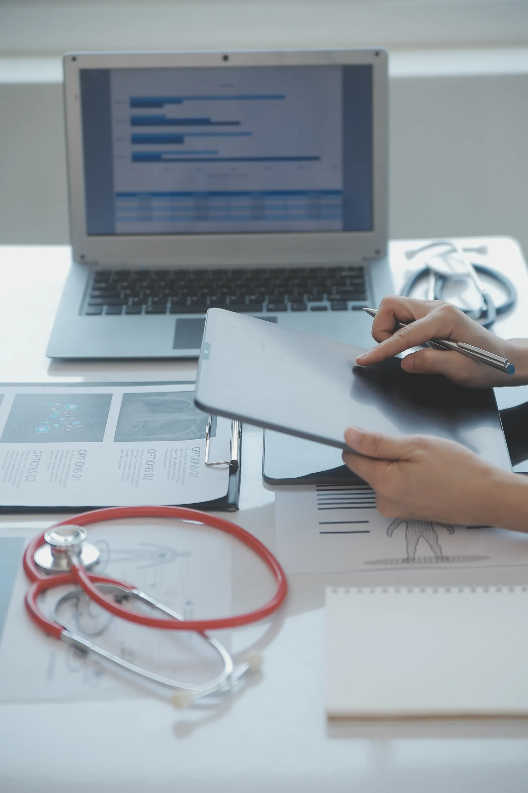Administrator holding a tablet and pen near a red stethoscope to perform exclusion screening software checks.