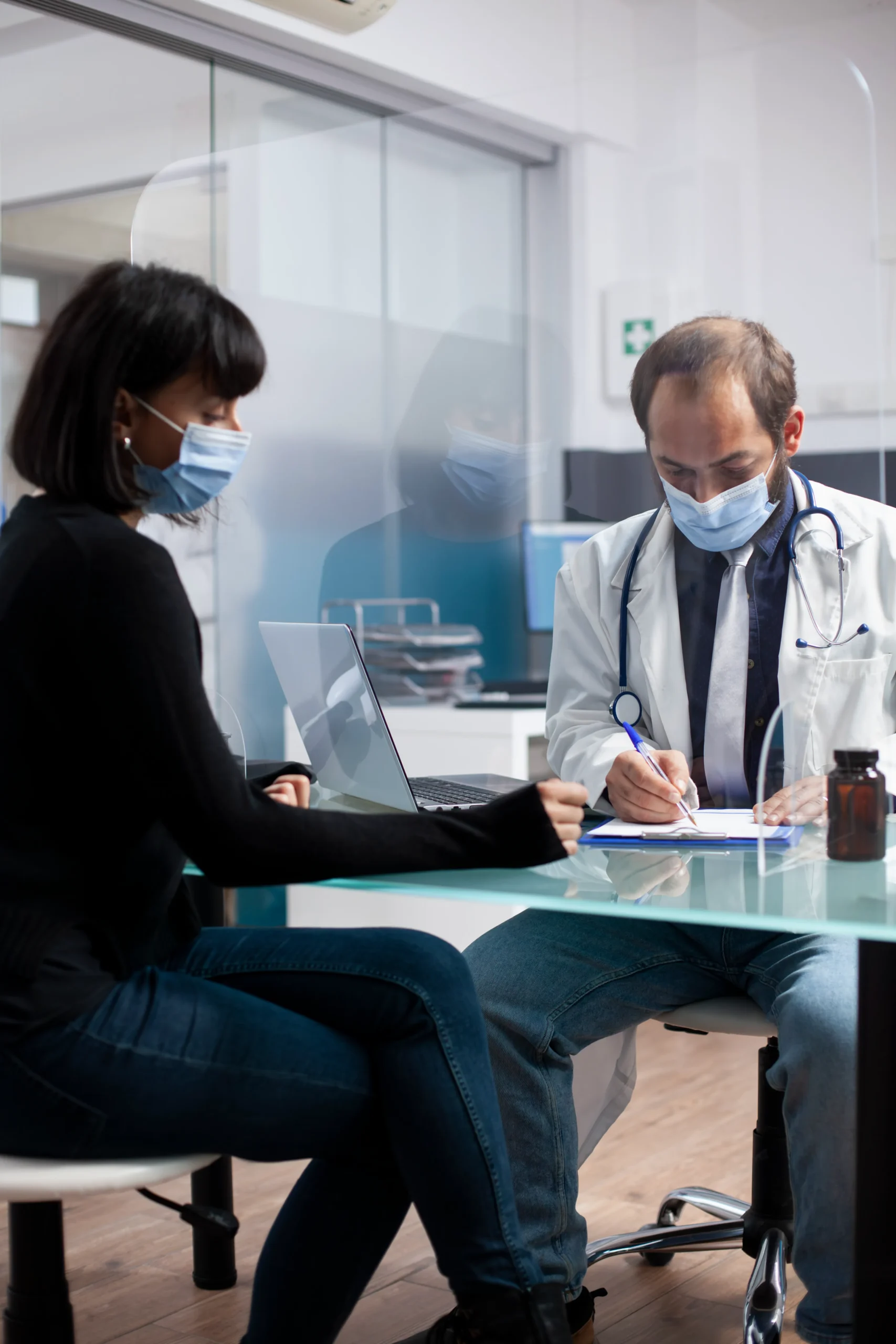 A doctor completing SAM screening paperwork during a patient intake consultation behind a clear barrier.