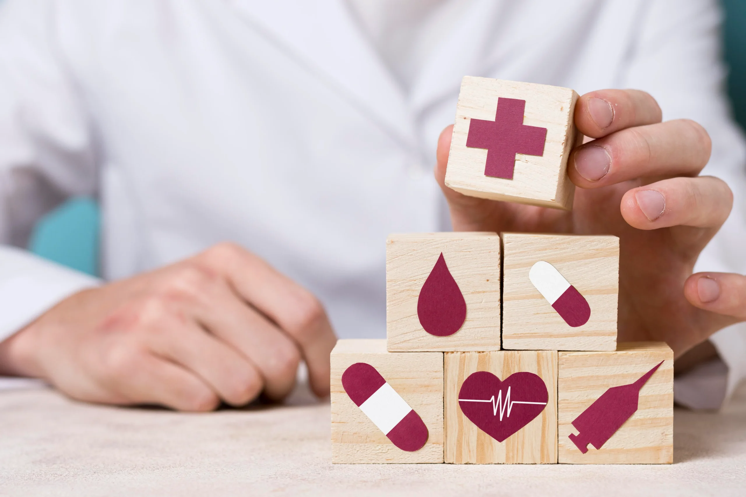 Hands arranging wooden blocks with medical icons to represent building compliance with OIG screening software.
